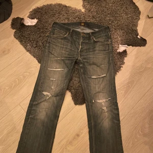 Jeans från Lee - Säljer ett par blå jeans från Lee med snygga slitningar. Storlek 30/32. Bra skick.