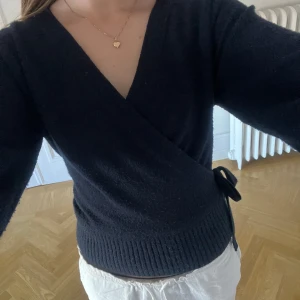 Blå omlottkofta med knyt i sidan - Mysig mörkblå omlottkofta med knyt i sidan. Koftan har lång ärm och en djup v-ringning, perfekt att styla över ett linne eller t-shirt. Materialet är stickat. Priset går att diskutera vid snabb affär❤️🫰🫶