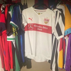 Vit Stuttgart fotbollströja Puma - Snygg vit fotbollströja från VfB Stuttgart med röd horisontell rand och klubbmärke på bröstet.