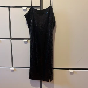 Svart glittrig klänning NLY One - Säljer en svart glittrig kortklänning från NLY One i storlek M. Klänningen har tunna axelband och är ärmlös med en snygg slits nertill. Materialet är glittrigt och ger en riktigt festlig känsla. Perfekt för dig som vill sticka ut med en cool look.
