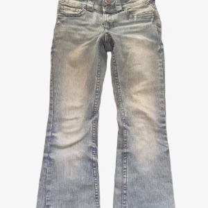 Ljusblå bootcut jeans med fickdetaljer - Snygga ljusblå jeans med bootcut passform och coola fickdetaljer bak med knappar. Jeansen har hög midja, dragkedja och dubbla knappar framtill. Perfekta för dig som gillar en retro vibe och vill sticka ut lite extra.