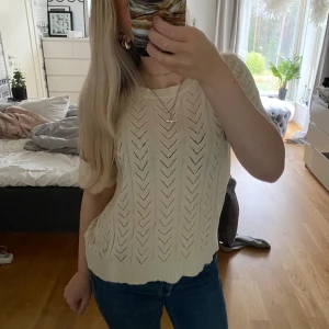 Ljusbeige stickad topp från Vila - Superfin ljusbeige stickad topp från Vila med korta ärmar och snyggt hålmönster i pilformat. Tillverkad i en mjuk mix av bomull och viskos, perfekt för vår och sommar. Sitter lite loose och har ribbade kanter nertill och vid ärmslut.