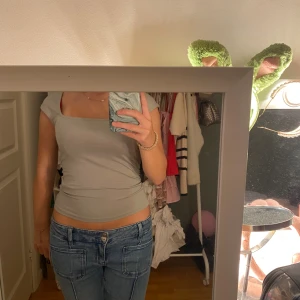 Grön T-shirt Gina tricot  - Säljer en ljustgrön tight topp med korta ärmar och snygg fyrkantig ringning. Toppen är croppad och sitter figurnära, perfekt till jeans eller kjol. Enkel och stilren design som passar till många olika looks.