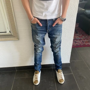 Tiger of Sweden Jeans - Snygga blå jeans från Tiger of Sweden i modellen Evolve, tillverkade i Italien. Jeansen har klassisk femficksdesign, orangea sömmar och en tvättad look med slitningar på låren. Passformen är rak med något smalare ben. Perfekta för dig som gillar en stilren och avslappnad vibe.