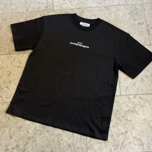 Maison Margiela svart t-shirt - Svart t-shirt från Maison Margiela med vit logotyptryck på bröstet i storlek M, T-shirten är i toppskick och fraktas inom 24h✅