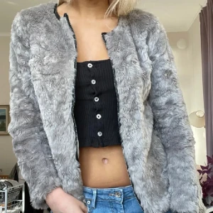 Grå pälsjacka från H&M Divided - Supermjuk och fluffig grå pälsjacka från H&M Divided. Jackan har lång ärm, rund halsringning och stängs med dragkedja framtill. Perfekt för dig som vill ha en mysig och trendig look under kyliga dagar. dock ett litet hål i armen men inget man tänker på!