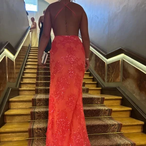 Glittrig korallfärgad långklänning - Säljer en glittrig korallfärgad långklänning med smala axelband och öppen rygg. Klänningen har en djup slits framtill och är täckt av paljetter som ger extra bling. V-ringad upptill och figurnära passform som framhäver siluetten. Perfekt för bal eller student.  34 i storleken men är som en 38-40 i storleken så den e stor i storleken!