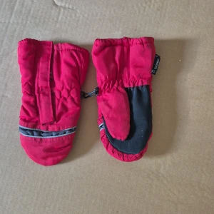 Röda tumvantar från Tuxer barn - Röda tumvantar från Tuxer med svart greppyta i handflatan och reflexdetalj på ovansidan. Vantarna har kardborreband vid handleden och elastisk mudd för bättre passform. Perfekta för kalla dagar.