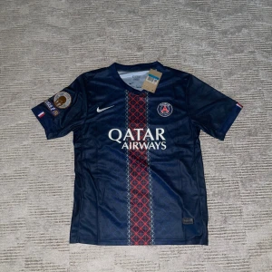 PSG matchtröja Nike Qatar Airways M - Snygg PSG fotbollströja från Nike med Qatar Airways som sponsor. Tröjan är marinblå med röd och vit grafisk rand i mitten, PSG-emblem på bröstet och mästarbadge på ärmen. Tillverkad i Dri-FIT material som andas. Perfekt för dig som älskar fotboll och vill sticka ut på planen. Kan skicka fler bilder privat. 