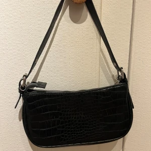 Axelväska i svart - Säljer denna lilla axelväska från HM Divided med croco-mönster och silverdetaljer💗Köpt för länge sen, tror inte den finns kvar att köpa på HM💞