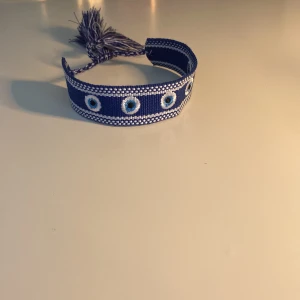 Blå tygarmband med ögonmönster som är hemmagjort!!! - Snyggt blått tygarmband med broderade ögonmönster som jag har gjort ensam hemma!! Med lite hjälp från min mamma…Säljer ett för 130kr och två för 180kr!!! Skriv för mer frågor!🙂