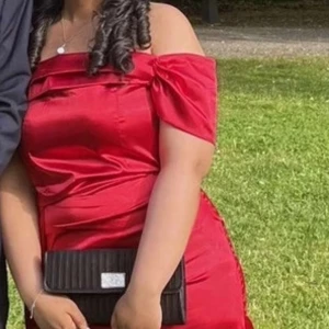 Röd off shoulder långklänning - Säljer en elegant röd långklänning med offshoulder-design och figurnära passform. Klänningen har en snygg omlott-detalj upptill och är tillverkad i ett glansigt material som ger en lyxig känsla. Perfekt för bal eller festliga tillfällen. Har sytt hos skrädderi!❤️