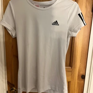 Vit Adidas t-shirt med svarta detaljer - Vit t-shirt från Adidas och är gjord i ett lätt och sportigt polyestermaterial som andas.