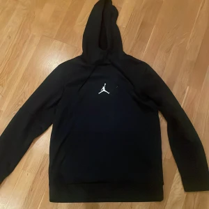 Svart Jordan hoodie med huva. - Svart hoodie från Jordan med klassisk Jumpman-logga broderad i vitt på bröstet. Tröjan har huva, långa ärmar och en relaxed passform. Fullt äkta!