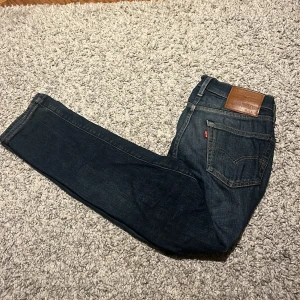 Levi's 511 mörkblå jeans W28 L30 - Snygga Levi's 511 jeans i mörkblå tvätt med klassisk femficksdesign och brunt läderpatch bak. Jeansen har en slim passform och är tillverkade i slitstarkt bomullsjeansmaterial. Perfekta för dig som gillar en modern och stilren look.