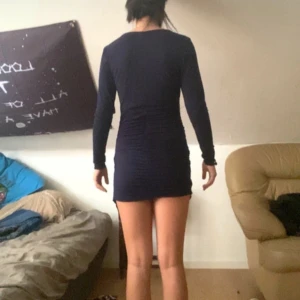 Mörkblå omlottklänning med v-ringning - Säljer en mörkblå kortklänning med lång ärm och snygg v-ringning. Klänningen har omlott-effekt framtill och är figurnära med lätt rynkade detaljer längs sidorna. Perfekt för dig som gillar en stilren och enkel look med en twist.