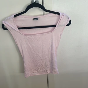 Ljusrosa ärmlös topp Gina Tricot XS - Säljer en ljusrosa topp från Gina Tricot i storlek XS. Toppen har en bred, fyrkantig urringning och är ärmlös med en slim passform. Materialet är mjuk bomull som känns skönt mot huden. Perfekt att styla med jeans eller kjol för en fräsch look.