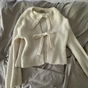 Vit stickad kofta med knytband - Superfin vit stickad kofta från Gina Tricot med ribbad struktur och två knytband framtill. Koftan har lång ärm och är croppad i modellen, perfekt att slänga över en topp. Enkel och stilren design som passar till mycket.