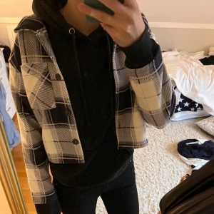 Rutig kappa/overshirt i fleece  - Säljer en väldigt skön overshirt i mjuk fleece med svart och vit rutigt mönster. Jackan har knappar framtill, två bröstfickor och lång ärm. Perfekt för lager-på-lager och ger en chill vibe till outfiten. Kappan är inte så gul som den ser ut att vara (se bild 4). 