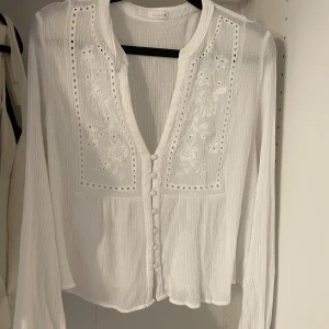 Vit broderad blus från Zara - Superfin vit blus från Zara med broderade detaljer och knappar framtill. Långärmad och i ett lätt, luftigt bomullstyg. V-ringad med spets och broderier som ger en romantisk vibe. Perfekt att styla med jeans eller kjol. Storlek M men skulle säga att den passar Xs/S