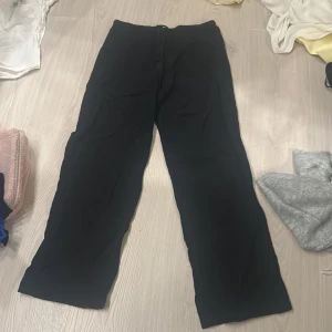 Svarta byxor från Gina Tricot - Svarta byxor från Gina Tricot med elastisk midja. Byxorna har en rak och lite loose passform, perfekta för en chill och enkel stil. Materialet känns mjukt och bekvämt, passar till många olika outfits.