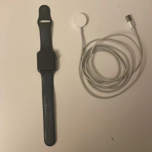 Apple Watch svart med laddare - Säljer en Apple Watch med svart silikonarmband. Vet inte riktigt hur gammal den är men den ligger på runt 2 år om inte lite till. Har använt den ett par gånger men inte mer än så, den har någon liten repa men som man knappast ser som ni kan se på bilden. Storlek 42mm case. Har ni frågor så tveka inte att säga till. Är öppen till bud🤝🏽
