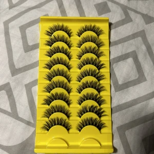 Flera par dramatiska lösögonfransar - Säljer ett set med 10 par svarta, fluffiga lösögonfransar i en gul förpackning. Fransarna har en tydlig volym och längd, perfekt för en intensiv look. De är täta och har en böjd form som ger ögonen extra lyft. Materialet är syntetiskt och mjukt.