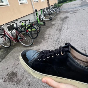 Lanvins - Säljer ett par svarta sneakers från Lanvin med snygg kontrast mellan blankt skinn på tån och mocka på sidorna. Skorna har svarta snören, silverfärgade öljetter och vit sula. Perfekta för dig som vill ha en stilren och lyxig look.