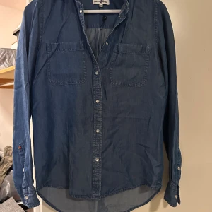 Blå jeansskjorta Hampton Republic strl: 34 - Snygg blå jeansskjorta från Hampton Republic med två bröstfickor och silvriga tryckknappar. Skjortan har lång ärm och klassisk krage, perfekt för en avslappnad och cool look. Materialet är mjukt och följsamt jeans.