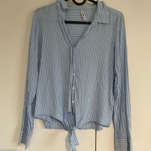 Blå- och vitrandig skjorta🤍 - Snygg blå skjorta med vita ränder i storlek XS. Skjortan har långa ärmar, klassisk krage och knäppning framtill. Nedtill finns en cool knyt-detalj som ger en avslappnad vibe. Perfekt för dig som gillar en fräsch och lätt stil. Använd 1 gång!🫶🏻