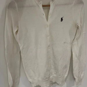 Vit kofta från Ralph Lauren  - Snygg vit kofta från Ralph Lauren i storlek XS. Klassisk design med knappar framtill och den ikoniska loggan broderad på bröstet. Långärmad och tillverkad i mjuk bomull, perfekt för lager-på-lager. Enkel att matcha med jeans eller kjol.    Passar S/XS