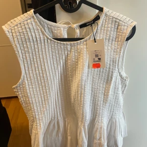 Vit ärmlös top från Bik Bok - Superfin vit top från Bik Bok med ärmlös design och vertikala sömmar framtill. Toppen har rund halsringning och knytning i nacken. 