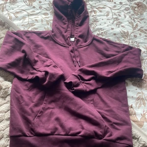 Vinröd hoodie med magficka - Mysig vinröd hoodie med stor huva och snörning. Tröjan har en klassisk magficka och ribbade muddar vid ärmslut och nederkant. Perfekt för chill dagar och enkel att matcha med jeans eller mjukisbyxor. Passar även perfekt nu till höst och kallare dagar