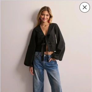 Svart  blus med knytning - Svart kortare blus från Nelly med långa, puffiga ärmar. Blusen har två knytband framtill och en djup v-ringning. Slutsåld & aldrig använd. Köpte för hösten men tyvärr aldrig blivit använd. 💞Ordinarie pris 299kr