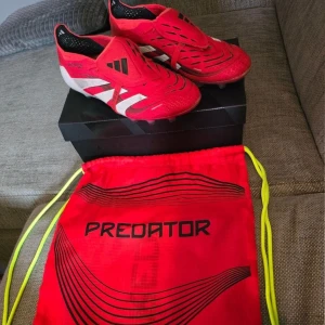 Adidas Predator Elite Fold-over Tongue AG Pure - Adidas Predator Elite Fold-over Tongue AG Pure Victory - Lucid Red/Vit/Svart Storlek EUR 43 1/3  Kommer med påse och kartong.  Har använts i några veckor innan sonen växte ur dom.  Fint skick! (Notera färgslitning på vänster fram)