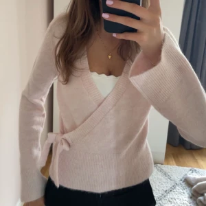 Ljusrosa omlottkofta med knyt - Superfin ljusrosa omlottkofta med knyt i sidan och breda ribbade muddar. Mjuk och mysig, perfekt för lager på lager. Passar både till jeans och kjol för en söt look. Aldrig använt 