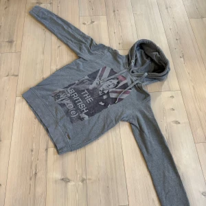 Sisley hoodie ”THE BRITHISH WILD(e) - Säljer en grå hoodie från Sisley med stort tryck på framsidan som föreställer Oscar Wilde och texten 'THE BRITISH WILD(e)'. Tröjan har huva med snörning och långa ärmar. Perfekt för dig som gillar unika prints!🙌🏼