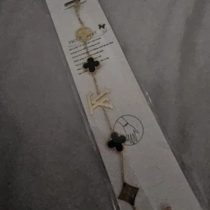  guldarmband - Snyggt armband i guldton med svarta och guldiga detaljer, prytt med LV-logga och ikoniska blommor. Kedjan är tunn och elegant, med flera olika former och symboler som ger en lyxig känsla. Perfekt accessoar för att lyfta din outfit.
