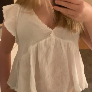 Vit blus med knyt från Nelly - Supersöt vit blus från Nelly i storlek 36. Blusen har v-ringning, volangärmar och en luftig, flowy passform. Baksidan har en öppen med knytband upptill. Super fin till jeans eller kostym byxor. Köpt för 250 för Nelly, nästan aldrig använd.