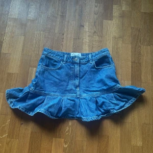 Jeanskjol med volang och hjärtfickor - Supersöt blå jeanskjol från Miss S med volangkant och två hjärtformade bakfickor. Kjolen har normal passform, bälteshällor och klassiska jeansdetaljer.  Kjolen har aldrig använts!