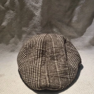 Rutig brun och beige keps från OUT360 - Snygg newsboy-keps från OUT360 i rutigt mönster med bruna och beige toner. Klassisk form med mjuk skärm och paneler, perfekt för dig som vill ha en retrovibe. Tillverkad i ullblandning som håller dig varm under kyliga dagar.