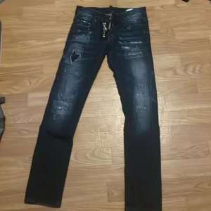 Mörkblå Dsquared2 jeans med slitningar - Snygga mörkblå jeans från Dsquared2 med coola slitningar och färgstänk. Jeansen har dragkedja med Dsquared2-detalj och klassisk femficksdesign. Smal passform och tillverkade i Italien. Perfekta för dig som gillar streetstyle och vill sticka ut.
