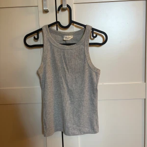 Grå ribbad linnetopp  - Säljer en enkel och stilren grå ribbad linnetopp från Gina tricot. Toppen är ärmlös med klassisk rund halsringning och har en tight passform.