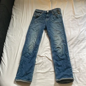 Blå jeans från Replay med raka ben - Säljer ett par klassiska blå jeans från Replay med snygg slitning och raka ben. Jeansen har fem fickor, läderpatch bak och tydliga kontrastsömmar. Perfekta för dig som gillar en tidlös och avslappnad look.