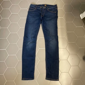 Mörkblå skinny jeans från Lee - Snygga mörkblå jeans från Lee med klassisk femficksdesign och kontrastsömmar. Modellen är slim och sitter tight hela vägen ner, perfekt för dig som gillar en smal siluett. Jeansen har dragkedja och knapp framtill samt Lee-logga på bakfickan.
