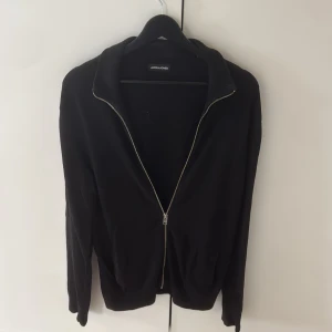 Svart fullzip med krage Jack & Jones - Svart tröja från Jack & Jones med hel dragkedja framtill och ribbad krage. Långärmad och i mjukt stickat material, perfekt för lager-på-lager. Enkel och stilren design som funkar till det mesta. Är strl S och något stor i storleken