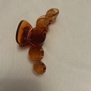 Brun hårklämma i retrostil - Snygg hårklämma i transparent brun plast med rundade former. Perfekt accessoar för att snabbt fixa frisyren och ge en cool retrovibe. Klämman har flera cirkelformade sektioner och en stadig metallfjäder för bra grepp.