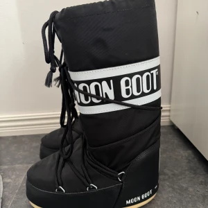 Svarta Moon Boots med snörning - Svarta Moon Boots med vit logga och snörning framtill. Höga skaft och bred passform, perfekta för vintern. Har haft på mig vid 1 tillfälle.💕