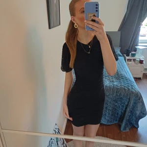 Svart spetsklänning från DIVIDED - Säljer en svart kortklänning från DIVIDED med puffiga kortärmar i spets och figurnära passform. Klänningen har ett diskret blommigt mönster i tyget och snygga rynkade detaljer framtill. Perfekt för dig som gillar stilrena. ❤️ storlek S