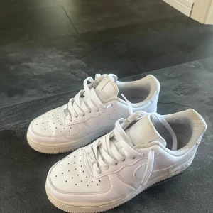 Nike Air Force 1 vita sneakers - Klassiska Nike Air Force 1 sneakers i helvitt skinn med perforerad tå, rund tå och platt sula. Snygg och tidlös modell med snörning och diskret Nike-logga på sidan och hälen. Perfekta för dig som gillar en clean och sportig look. Har använts mycket men har försökt rengöra dom, även bytt skosnöre.